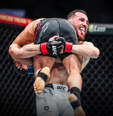 Merab picking up an Olympic Gold Medalist in freestyle wrestling and walking towards Mark Zuckerberg 