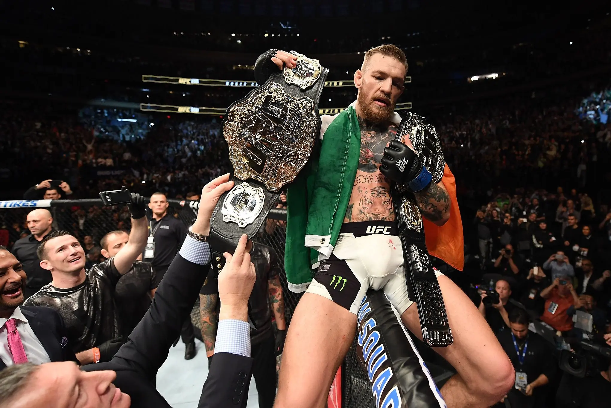 Conor McGregor celebrates on the cage with his UFC Lightweight and Featherweight title belts. Credit: Bleacher Report.